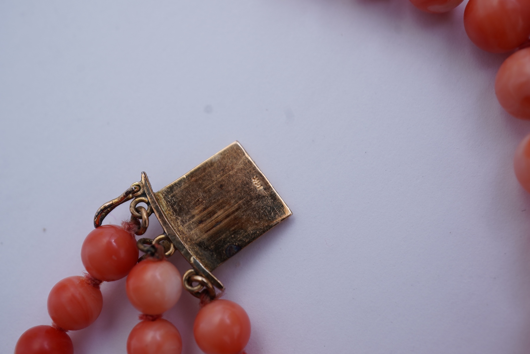 A coral necklace, composed of three strands of coral beads measuring approximately 5.1-6.6mm diameter, to a gold clasp set with a coral cabochon and brilliant-cut diamonds, mounted in gold, length 45.5cm, stamped 14K, ca